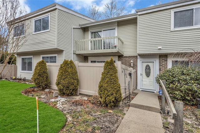 view of front of property with a front yard, brick siding, fence, and a balcony