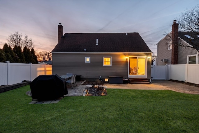 back of property at dusk with entry steps, a patio area, a yard, and a fenced backyard