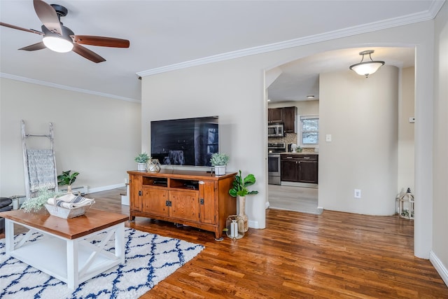 living room featuring arched walkways, baseboards, wood finished floors, and crown molding