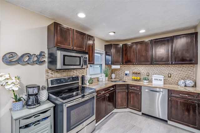 kitchen with a sink, dark brown cabinets, appliances with stainless steel finishes, backsplash, and light stone countertops