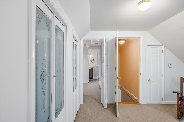 hall with lofted ceiling, light carpet, and baseboards