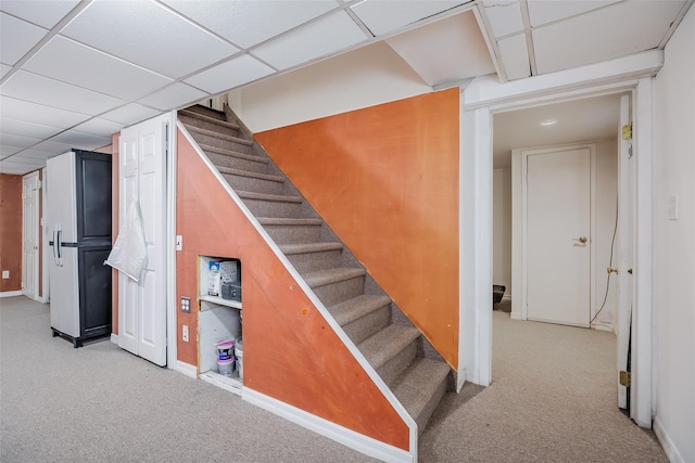 stairway featuring carpet floors, a drop ceiling, and baseboards