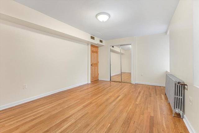 unfurnished bedroom with visible vents, baseboards, a closet, light wood finished floors, and radiator heating unit