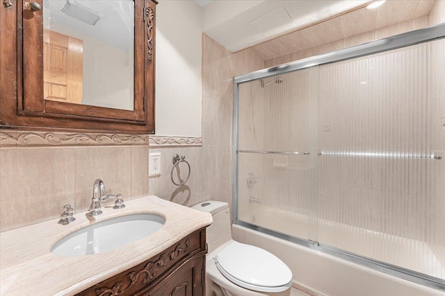 bathroom featuring tile walls, toilet, wainscoting, enclosed tub / shower combo, and vanity