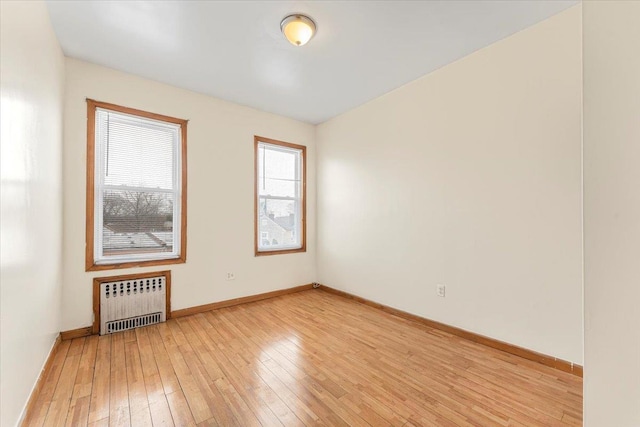 unfurnished room featuring radiator, light wood-type flooring, and baseboards