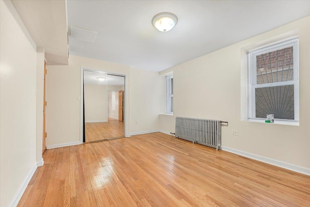 unfurnished room with light wood-style floors, radiator, and baseboards