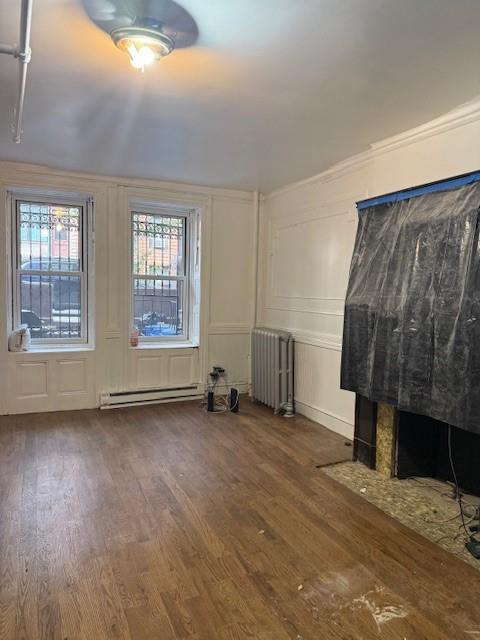 412 W 146th St, New York Manhattan, NY 10031 - unfurnished living room with a baseboard heating unit, radiator heating unit, a decorative wall, wood finished floors, and plenty of natural light