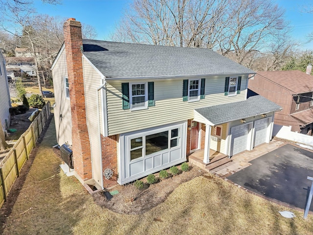 view of front of home featuring driveway, a chimney, fence, and roof with shingles