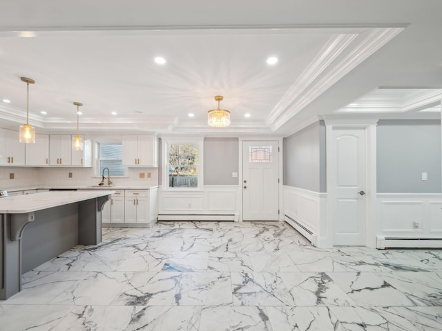 kitchen with a tray ceiling, a wainscoted wall, light countertops, baseboard heating, and white cabinets