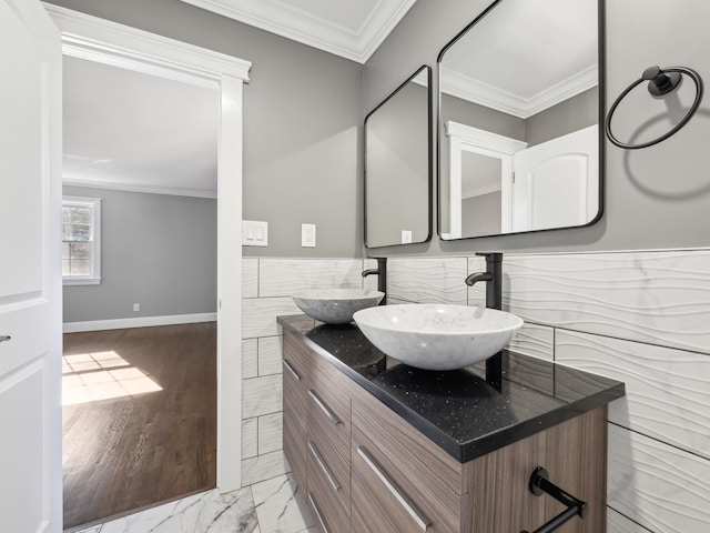 bathroom with marble finish floor, ornamental molding, a sink, and tile walls