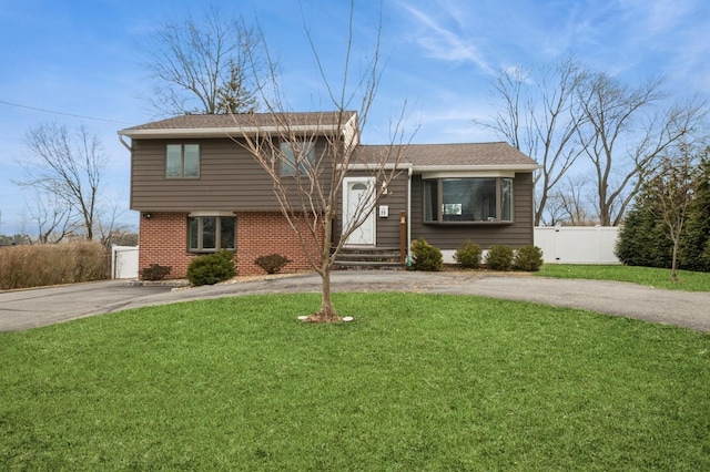 split level home featuring brick siding, a gate, fence, driveway, and a front lawn