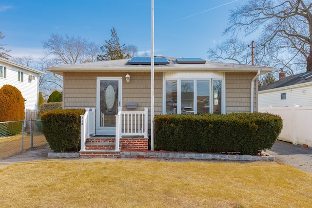 bungalow-style house featuring fence, a front lawn, and solar panels