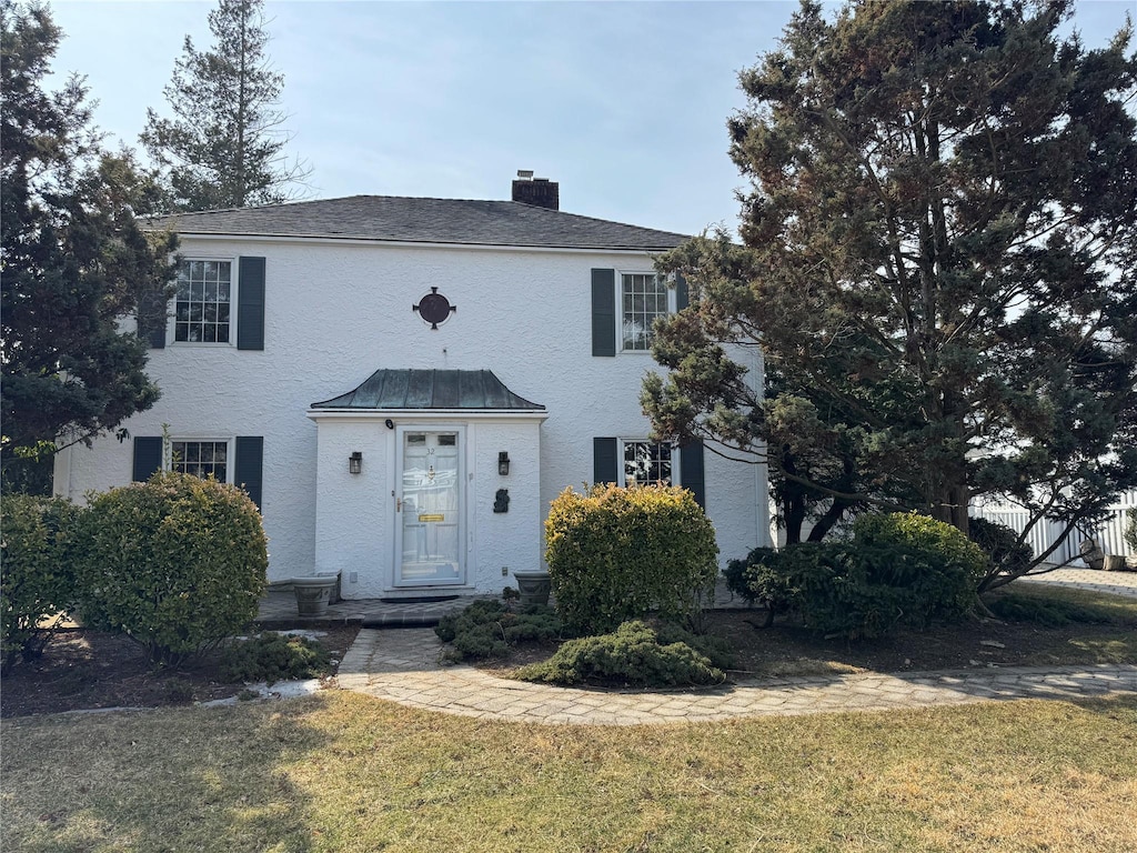 colonial-style house with fence, a chimney, and a front lawn