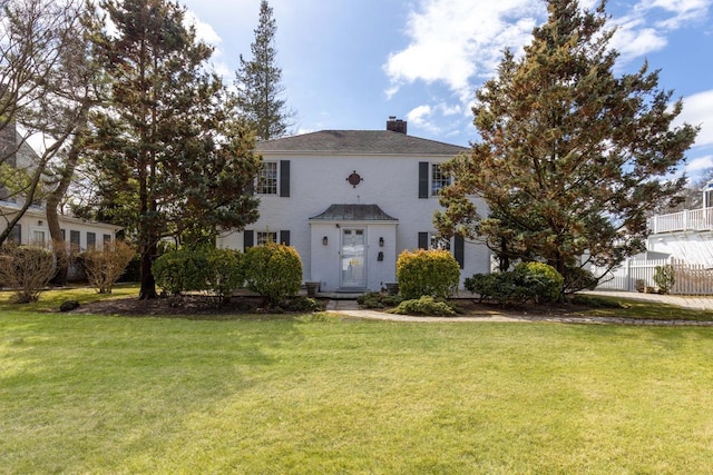 colonial-style house with a chimney, fence, and a front yard