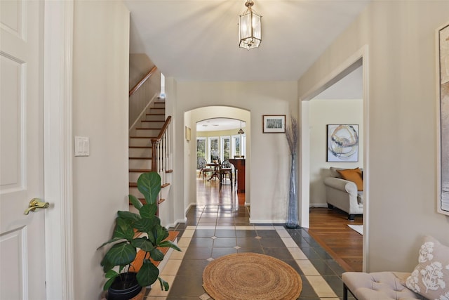 foyer entrance with stairway, dark tile patterned floors, baseboards, and arched walkways