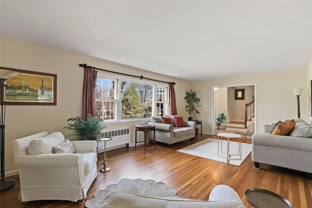 living area with stairway, baseboards, radiator, and wood finished floors