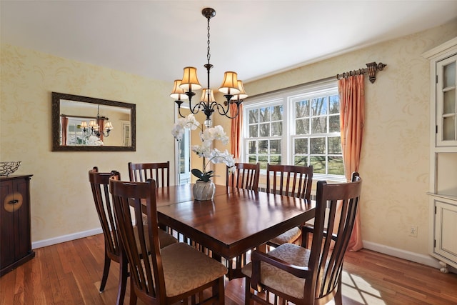 dining area with wallpapered walls, hardwood / wood-style flooring, a notable chandelier, and baseboards