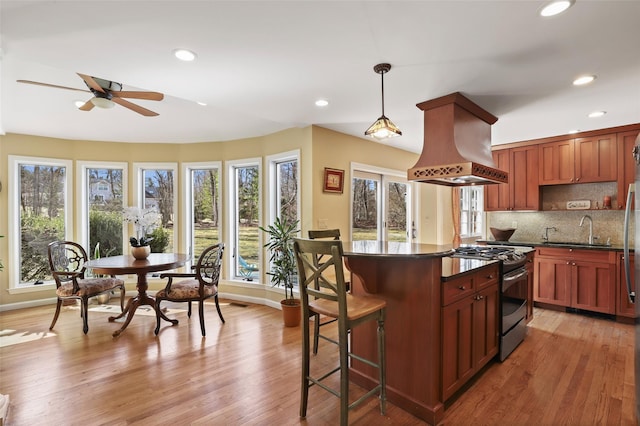 kitchen with a sink, dark countertops, island range hood, ceiling fan, and stainless steel gas range