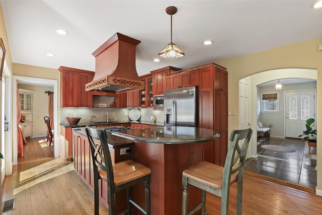 kitchen featuring light wood-style floors, island exhaust hood, arched walkways, and appliances with stainless steel finishes