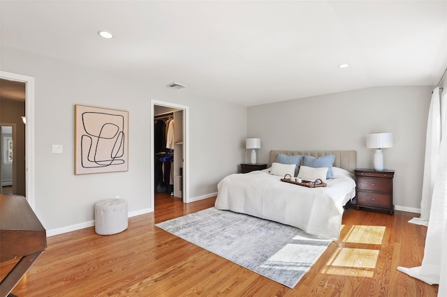 bedroom with a walk in closet, lofted ceiling, wood finished floors, and baseboards