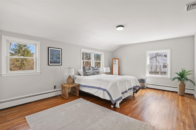 bedroom featuring visible vents, wood-type flooring, lofted ceiling, and a baseboard heating unit