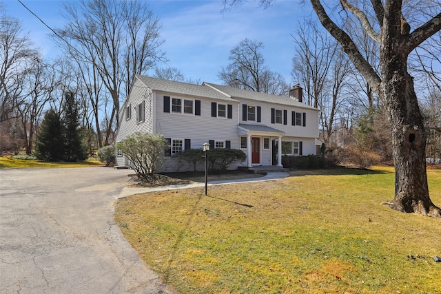 view of front of home with aphalt driveway, a front lawn, roof with shingles, and a chimney