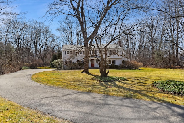 view of front of home with driveway, a chimney, and a front lawn