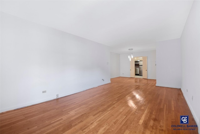 unfurnished living room featuring baseboards, light wood finished floors, and an inviting chandelier