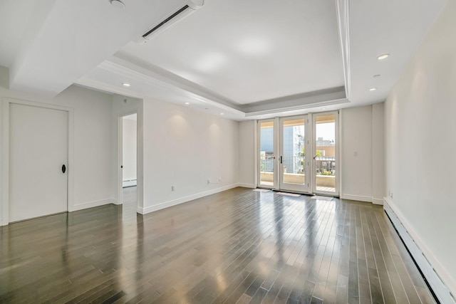 empty room featuring a baseboard heating unit, wood finished floors, visible vents, baseboards, and a tray ceiling