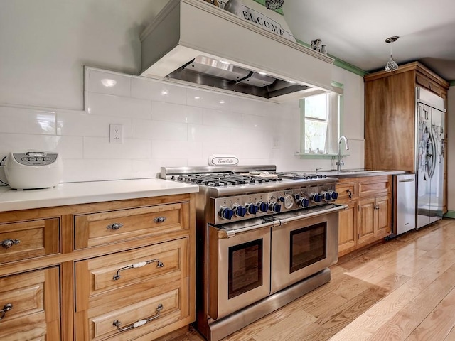 kitchen featuring tasteful backsplash, premium appliances, light wood-style flooring, under cabinet range hood, and a sink