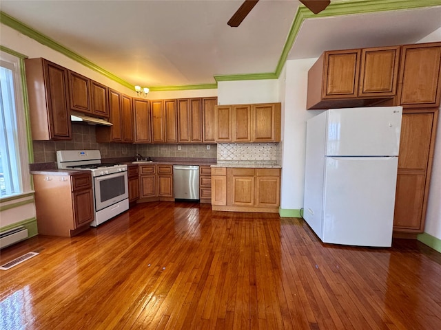 kitchen featuring under cabinet range hood, white appliances, visible vents, dark wood-style floors, and tasteful backsplash