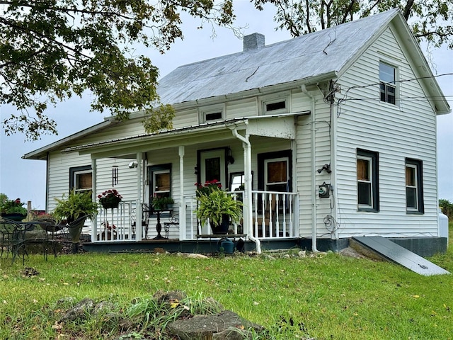 view of front facade with covered porch, a chimney, and a front yard