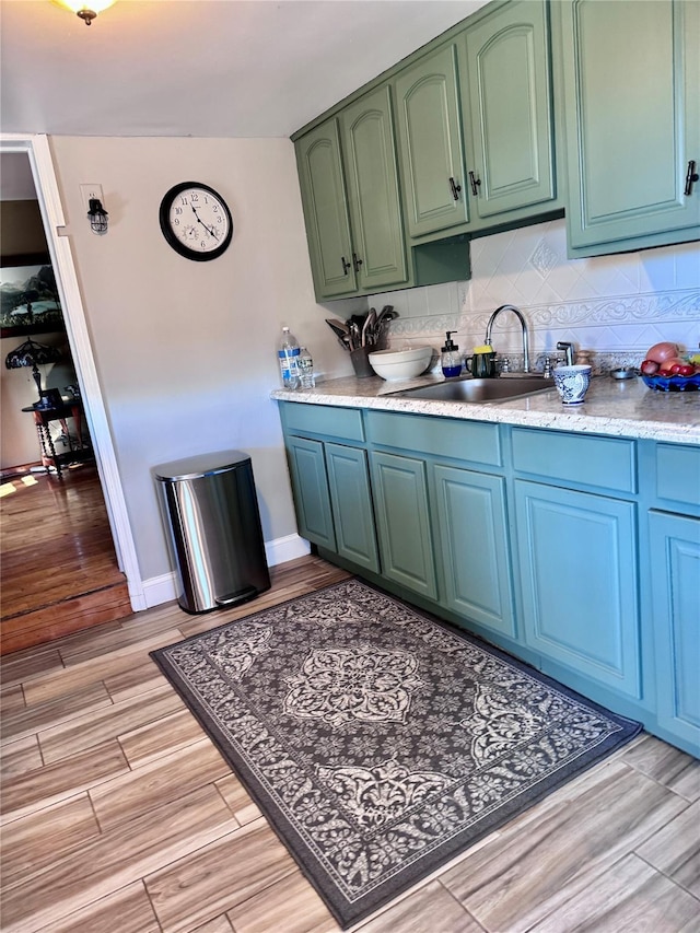 kitchen with baseboards, decorative backsplash, light wood-style floors, green cabinets, and a sink