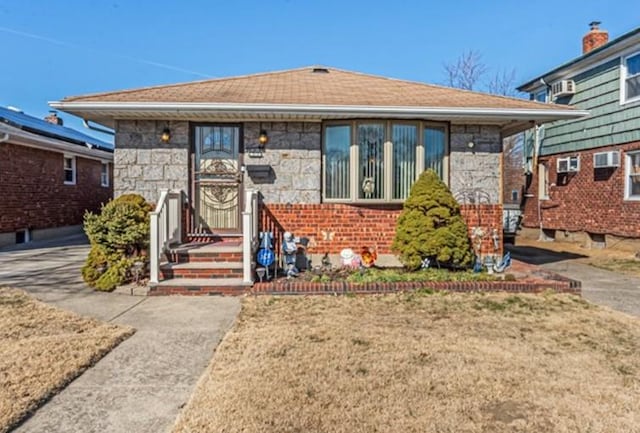 bungalow-style home with brick siding, stone siding, and a front yard