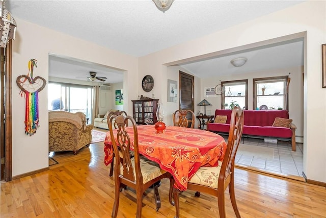 dining space featuring baseboards, a wall mounted air conditioner, a textured ceiling, and light wood finished floors