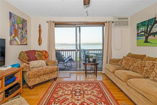 living room featuring a wall mounted air conditioner, a water view, a textured ceiling, and light wood finished floors