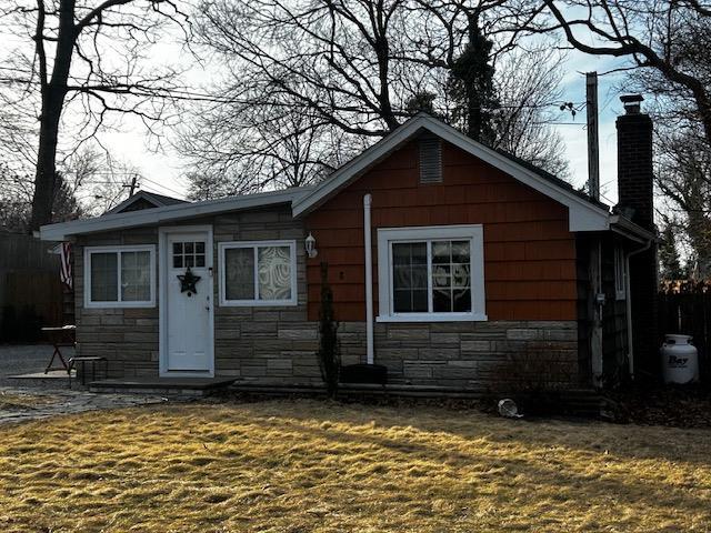 view of front of house featuring stone siding, a chimney, and a front lawn