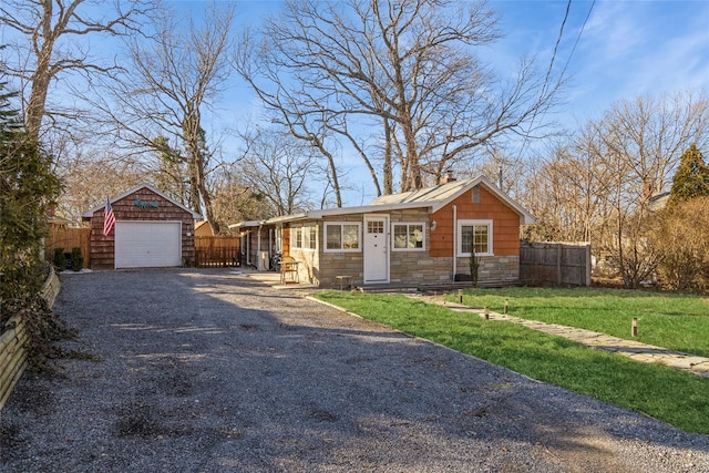 view of front of home with a front yard, fence, gravel driveway, an outdoor structure, and a garage