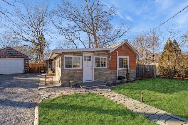 view of front of home featuring a front lawn, stone siding, fence, gravel driveway, and an outdoor structure