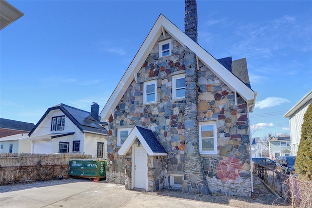 view of front facade with stone siding, a chimney, and fence