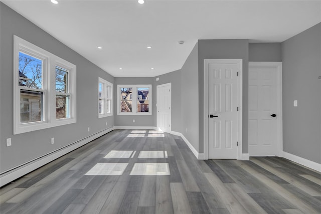 unfurnished living room featuring baseboards, a baseboard heating unit, wood finished floors, and recessed lighting