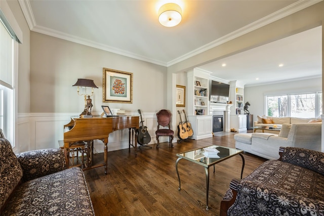 living room with a glass covered fireplace, a wainscoted wall, crown molding, and wood finished floors