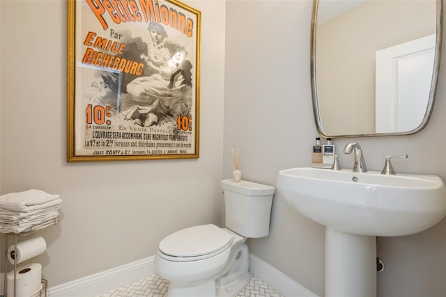 half bath featuring toilet, baseboards, a sink, and tile patterned floors