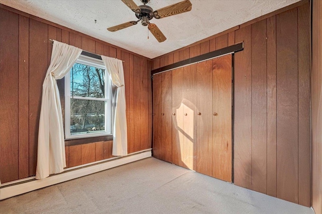 unfurnished bedroom featuring wood walls, baseboard heating, and carpet floors