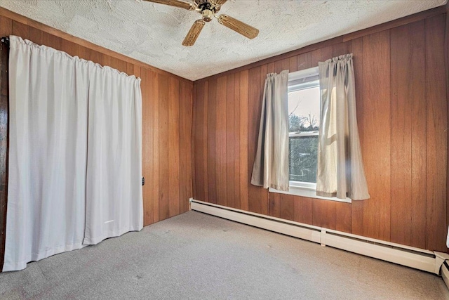 carpeted empty room featuring a textured ceiling, wooden walls, baseboard heating, and ceiling fan