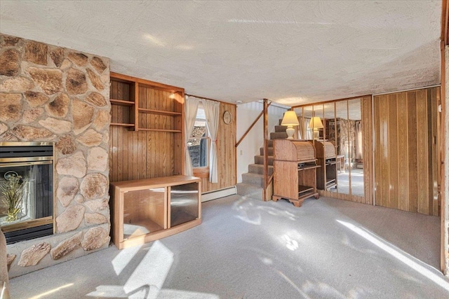 unfurnished living room featuring stairway, wooden walls, a fireplace, a textured ceiling, and a baseboard heating unit