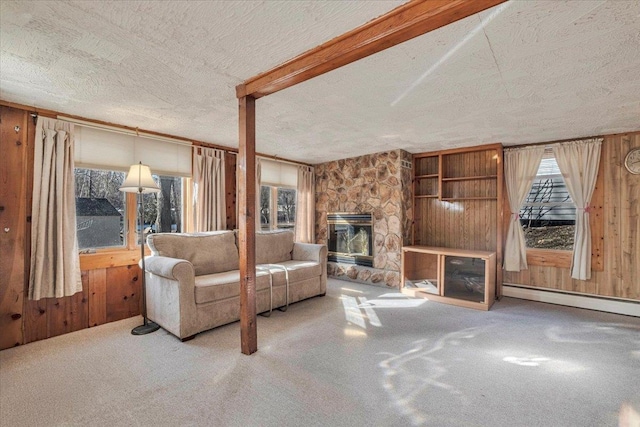 carpeted living room featuring a stone fireplace, wood walls, a textured ceiling, and a baseboard heating unit