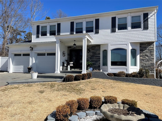 view of front of home with a garage, driveway, stone siding, covered porch, and a front yard