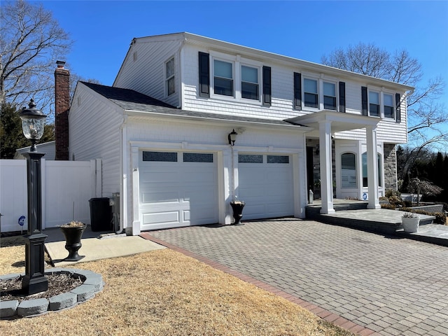 traditional-style house with a garage, decorative driveway, and fence