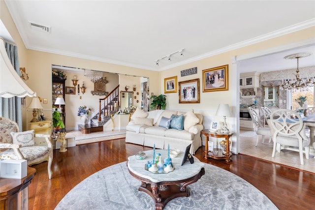 living area with wood finished floors, crown molding, stairway, and an inviting chandelier